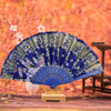 Elegant folding fan with traditional Chinese design featuring blue and green floral patterns displayed on a wooden stand.