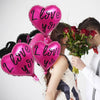A set of ten pink and black heart-shaped balloons is held by a couple.