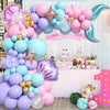 A pink and blue balloon garland arch set for a birthday party featuring various colored balloons and tissue paper flowers.