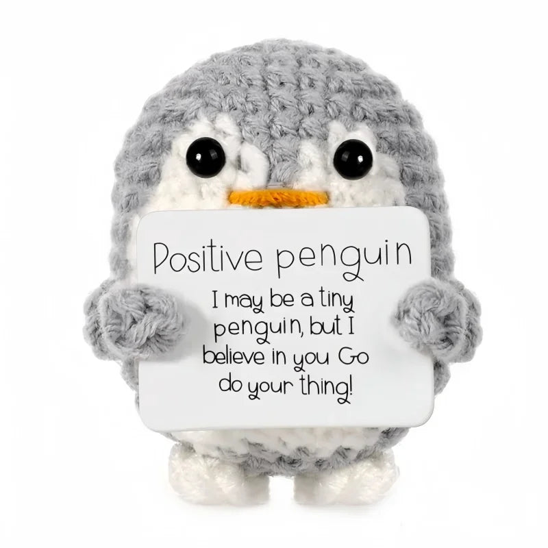 A gray crocheted penguin toy holding a white card with the message I may be a tiny penguin but I believe in you go do your th