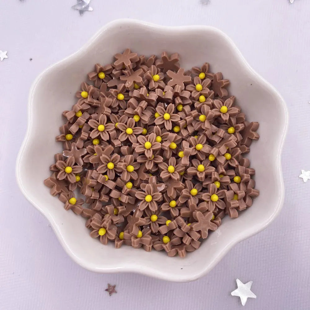 A small white dish filled with brown resin flower gems with yellow centers for crafts and DIY projects