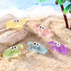 A set of luminous resin mini crab decor figures in yellow, pink, and purple resting on a sandy beach.