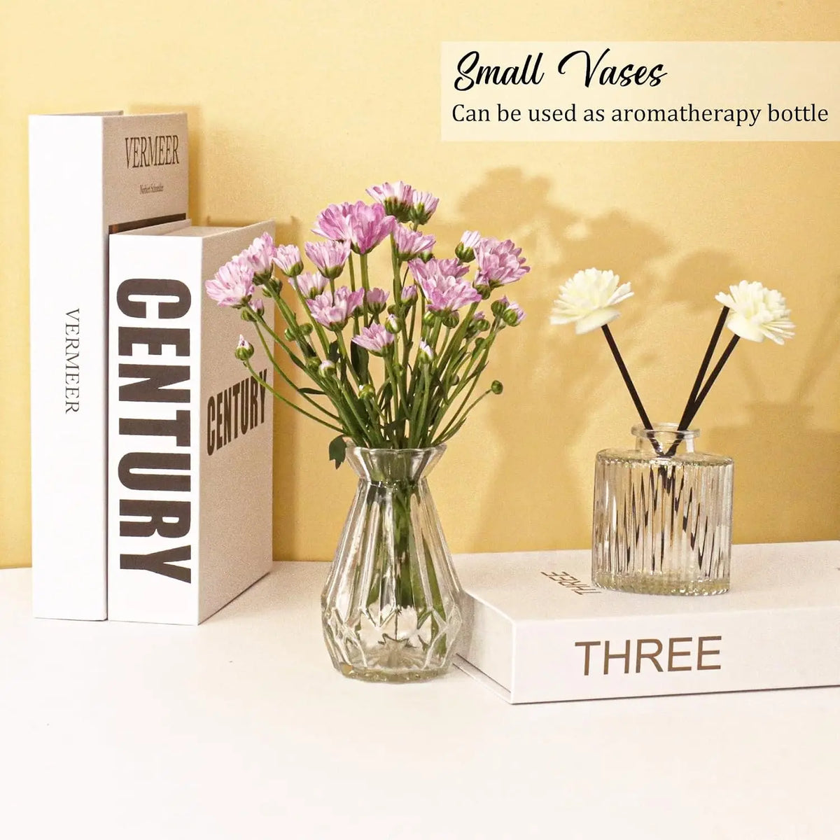 A set of three small vintage bud glass vases with pink and white flowers displayed on a light surface.