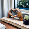 A heart-shaped wooden sculpture rests on a light-colored surface next to a succulent plant by a window.
