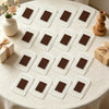 A collection of square photo frame magnets with brown photos arranged on a white tablecloth.