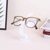 A pair of round, gold-rimmed glasses resting on a white minimalist display stand.