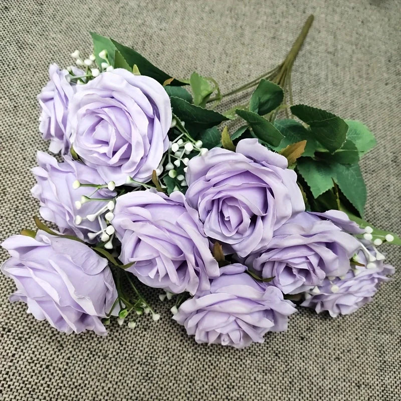 A bouquet of light purple silk peonies with green leaves and small white filler flowers.