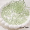 A magnifying glass shows small, round, translucent green glass spacer beads scattered on a white dish.