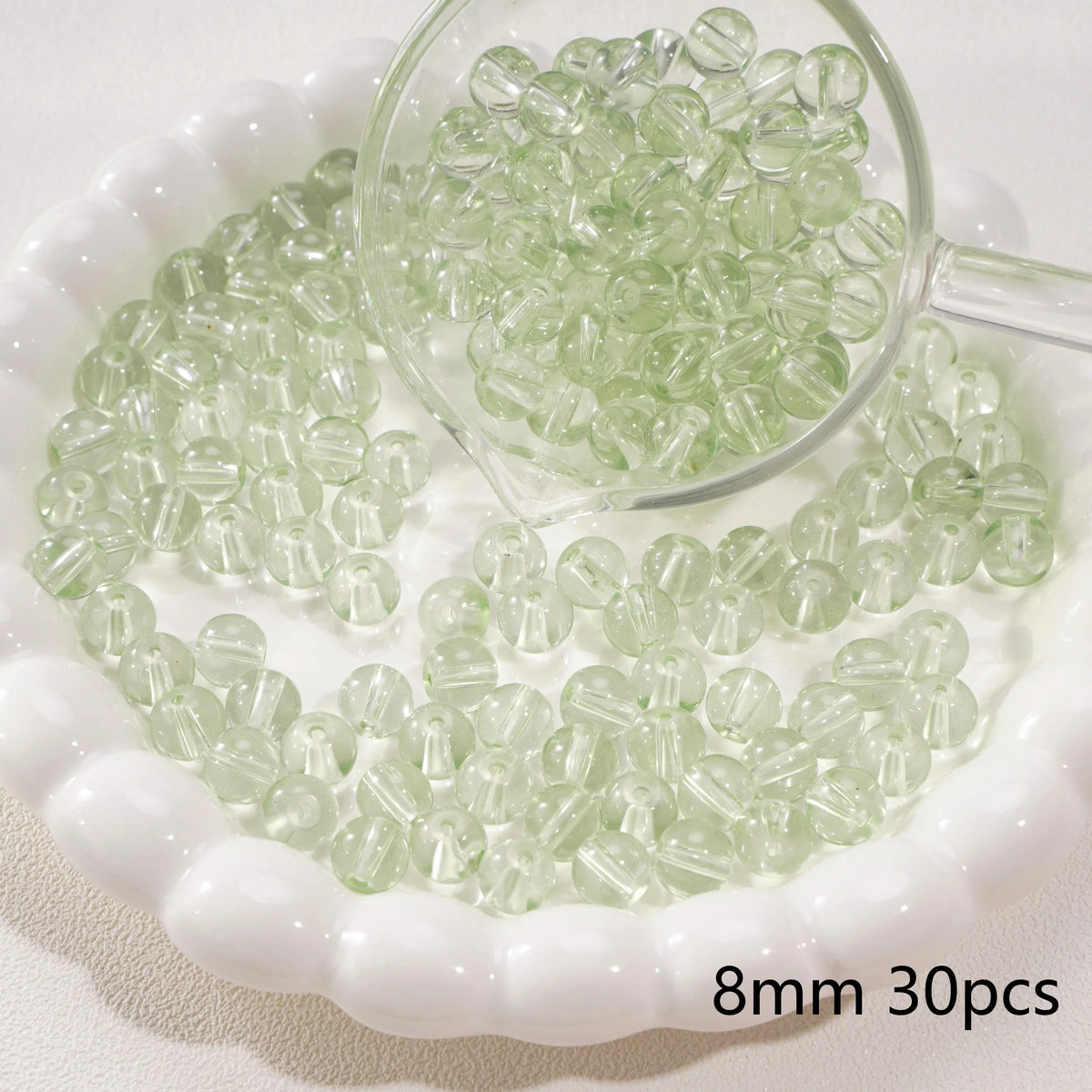 A magnifying glass shows small, round, translucent green glass spacer beads scattered on a white dish.