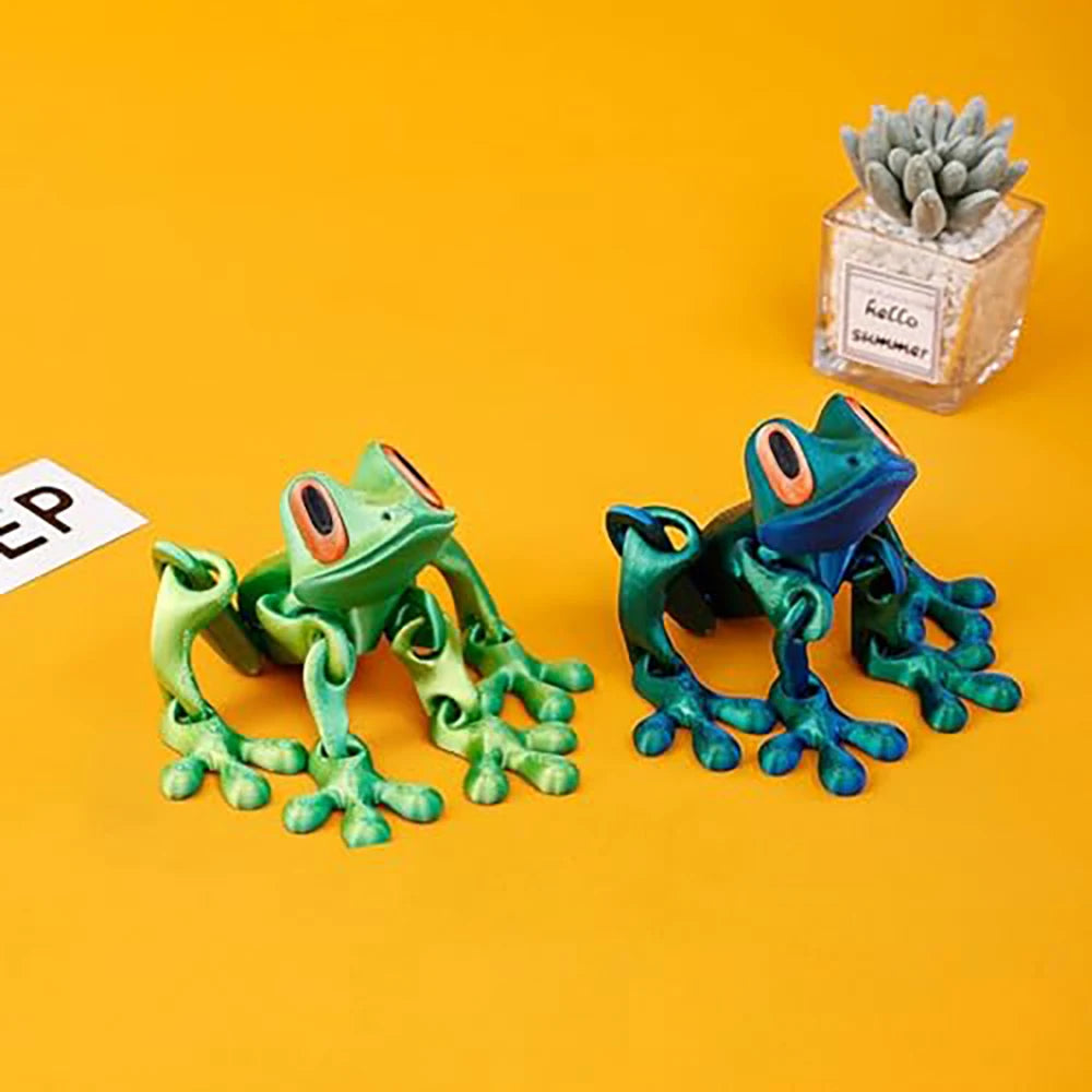 A bright green articulated 3D printed frog magnet with large eyes is displayed next to a small succulent plant.