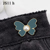 A close-up of a teal butterfly button with a pearl center attached to black denim fabric.