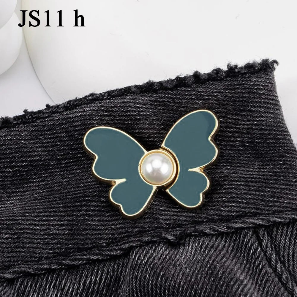 A close-up of a teal butterfly button with a pearl center attached to black denim fabric.