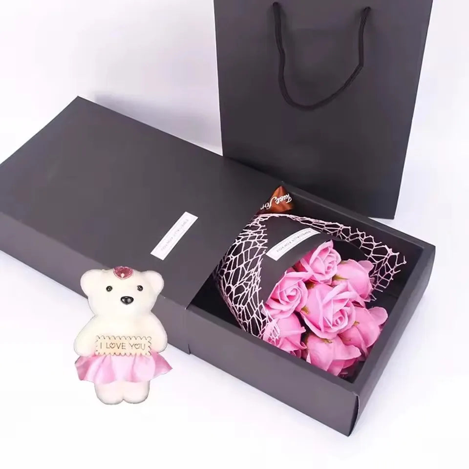 A gift box containing a fragrant soap rose bouquet and a plush bear, presented in a dark gray box.
