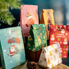 A collection of pink, yellow, and red Christmas-themed kraft paper gift bags with seal stickers displayed on a surface.