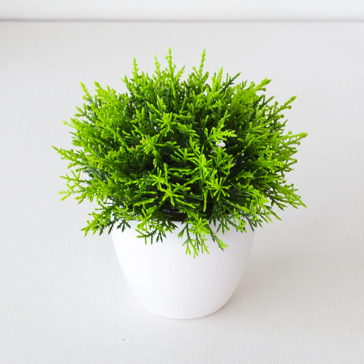 Un vibrant arbre bonsai artificiel vert dans un pot blanc, exposé sur une surface blanche.