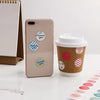 Ein beige Smartphone zeigt runde Dankessticker auf der Rückseite neben einer braunen Papptasse für Kaffee.