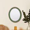 An oval wall mirror with a green frame and intricate lace design hanging on a light-colored wall.