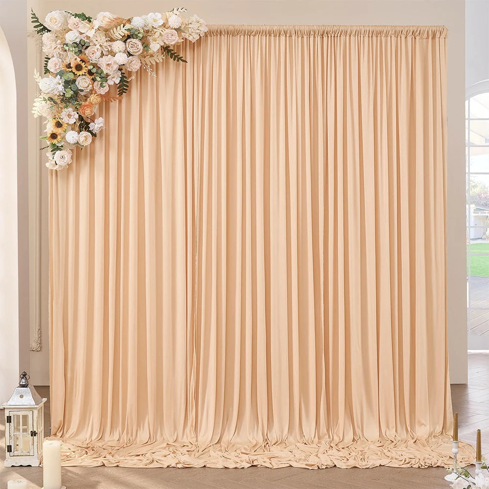 A floor-to-ceiling beige pleated fabric backdrop with floral arrangements used as decoration.