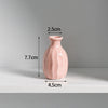 A pink ceramic mini vase with a rounded body and narrow neck, shown against a light gray background.
