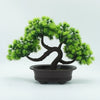 An artificial bonsai pine tree with dark bark and bright green needles planted in a black pot.