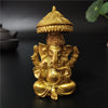 A golden bronze statue of Ganesha Buddha seated in a meditative pose with an ornate crown.