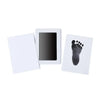 A white frame displaying a black handprint and footprint on a card, part of an inkless baby keepsake kit.