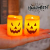 A hand holds two glowing orange Halloween jack-o'-lantern LED candles against a blurred background.
