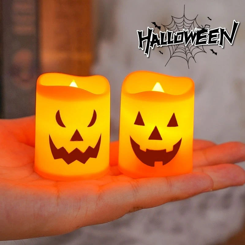 A hand holds two glowing orange Halloween jack-o'-lantern LED candles against a blurred background.