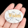 A hand holds a round white marble stone with the word Wisdom engraved on it.