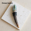 An Ocean Jasper scepter wand with a green crystal top and dark wood handle resting on a white card.