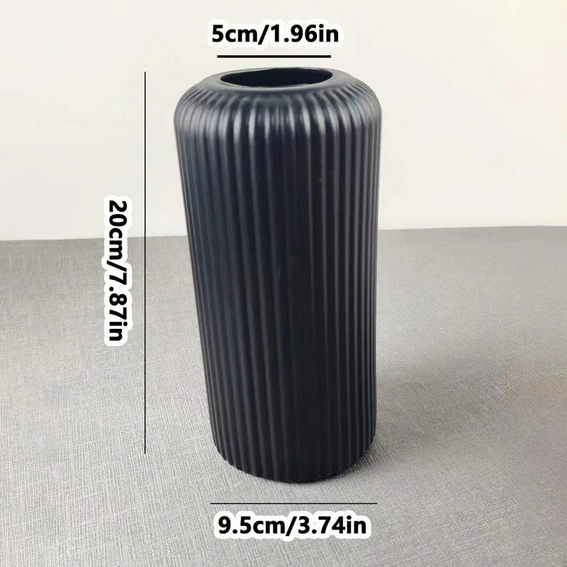 Eine hohe, schwarze, geriffelte Keramik-Optik Kunststoffvase vor neutralem Hintergrund.