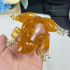 A translucent amber crystal frog resin craft decoration is held in a hand against a white background.