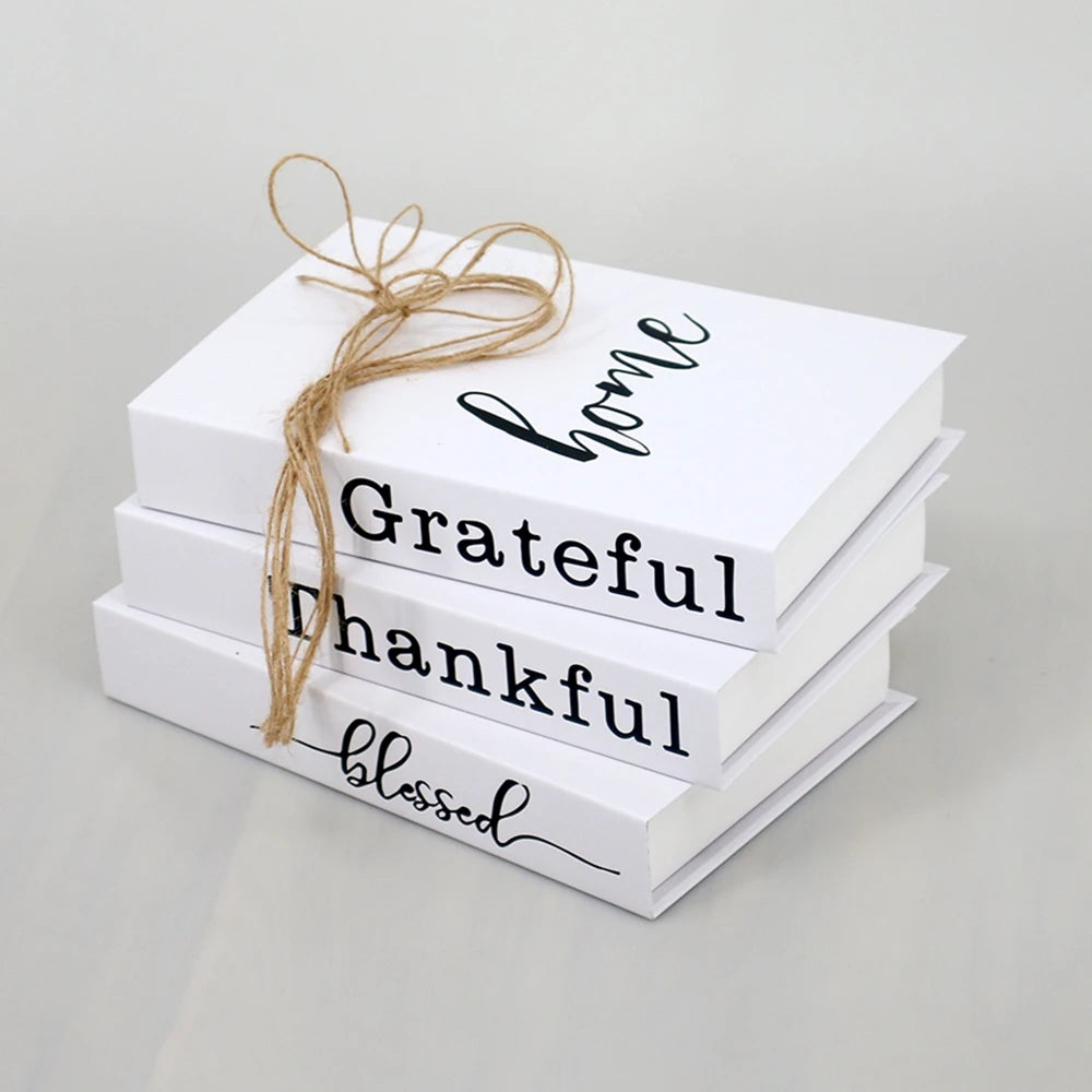 A set of three white decorative fake books with black script text and twine tied on top.