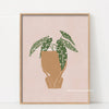 Wall art featuring a watercolor illustration of a philodendron plant in a terracotta pot on a light pink background.