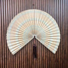 Handwoven bamboo wall fan decor with a light beige and brown striped fan featuring a dark tassel.