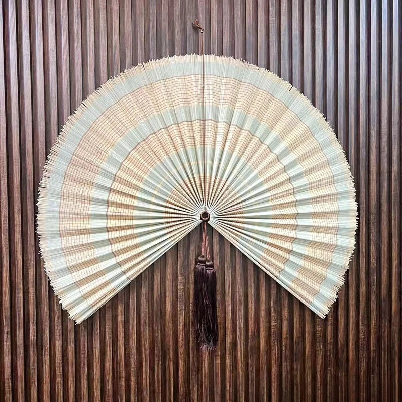 Handwoven bamboo wall fan decor with a light beige and brown striped fan featuring a dark tassel.