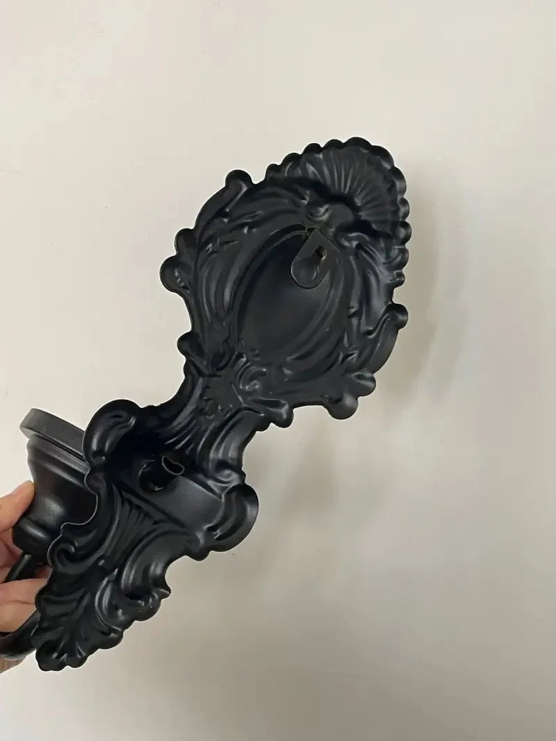 A black vintage wrought iron wall-mounted candle holder with an ornate, scrolled design.