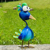 A vibrant blue metal peacock garden sculpture with bright green crests standing on a gray surface.