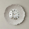 A round silver wall clock with a textured, sunburst-like metal frame and a gold-toned watch face.