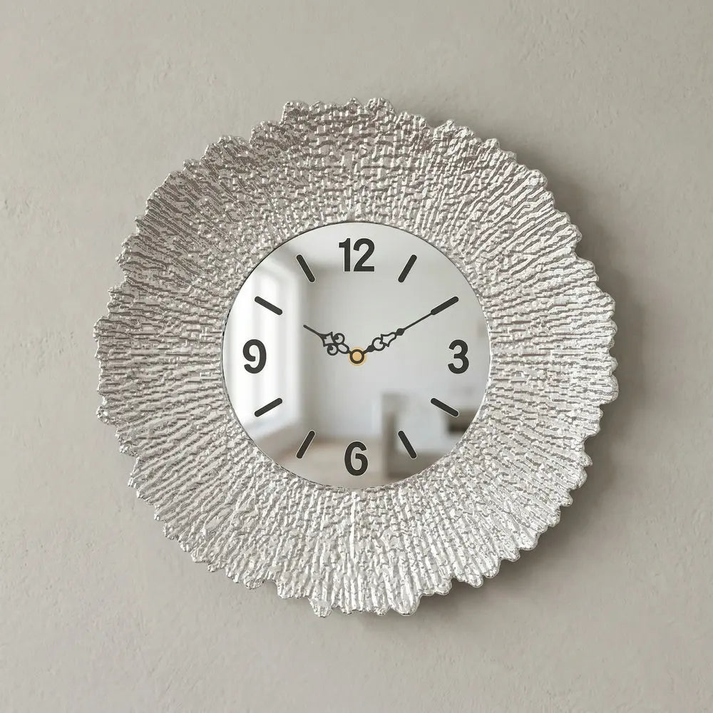 A round silver wall clock with a textured, sunburst-like metal frame and a gold-toned watch face.