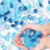 A hand holds a pile of blue and clear decorative crushed diamond acrylic pebbles.