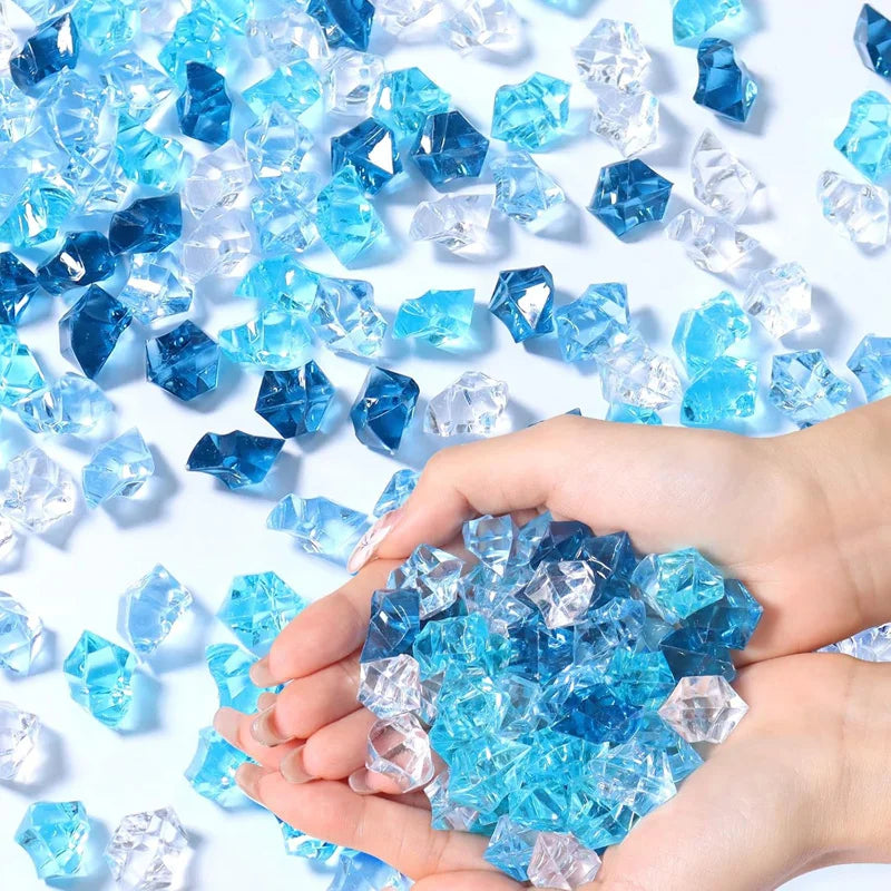 A hand holds a pile of blue and clear decorative crushed diamond acrylic pebbles.