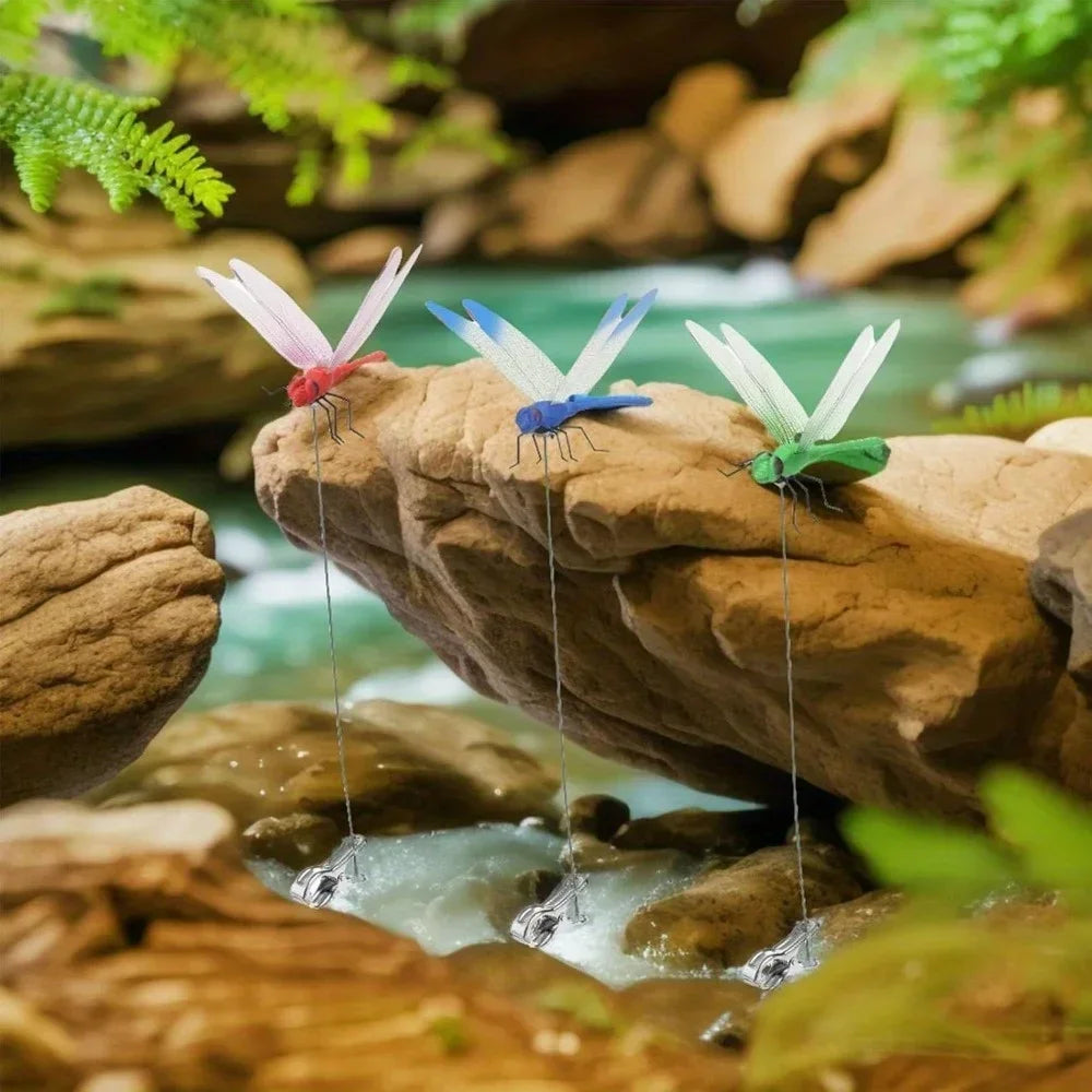 Colorful dragonfly hat clips are attached to rocks in a natural garden setting.