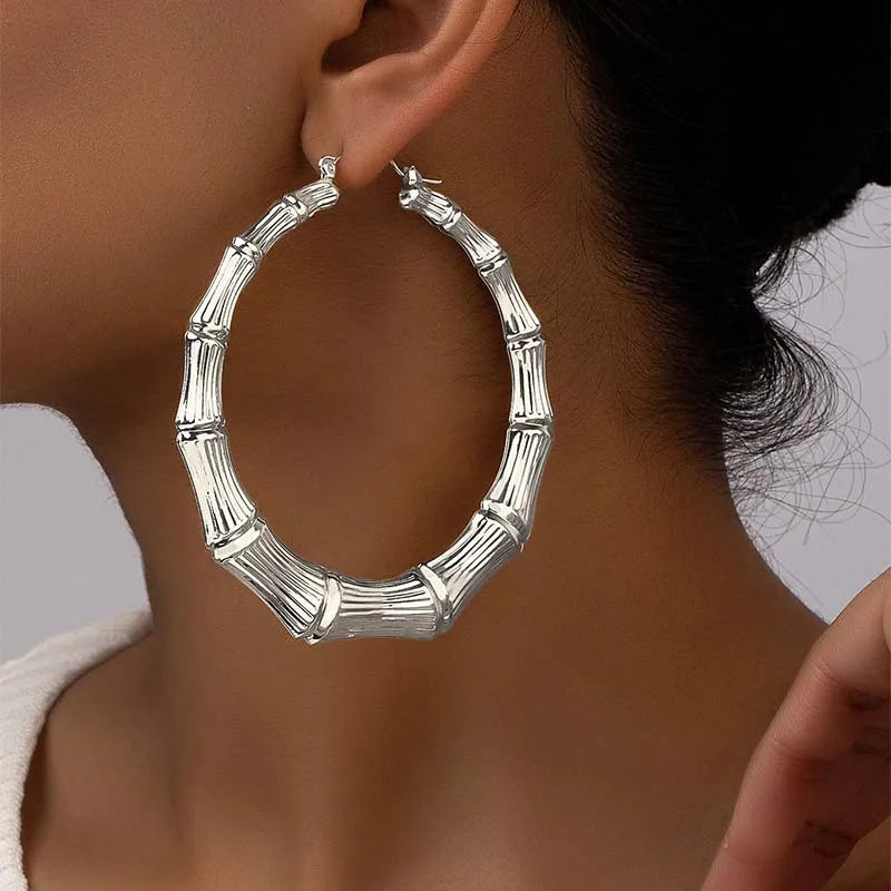Silver bamboo hoop earrings worn on a woman's ear.