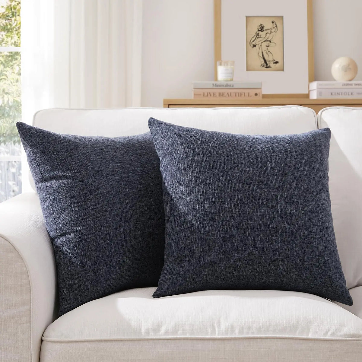Two dark gray linen pillows resting on a white sofa with a framed picture in the background.