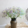 A bouquet of artificial baby's breath flowers in shades of purple and white arranged in a dark vase.