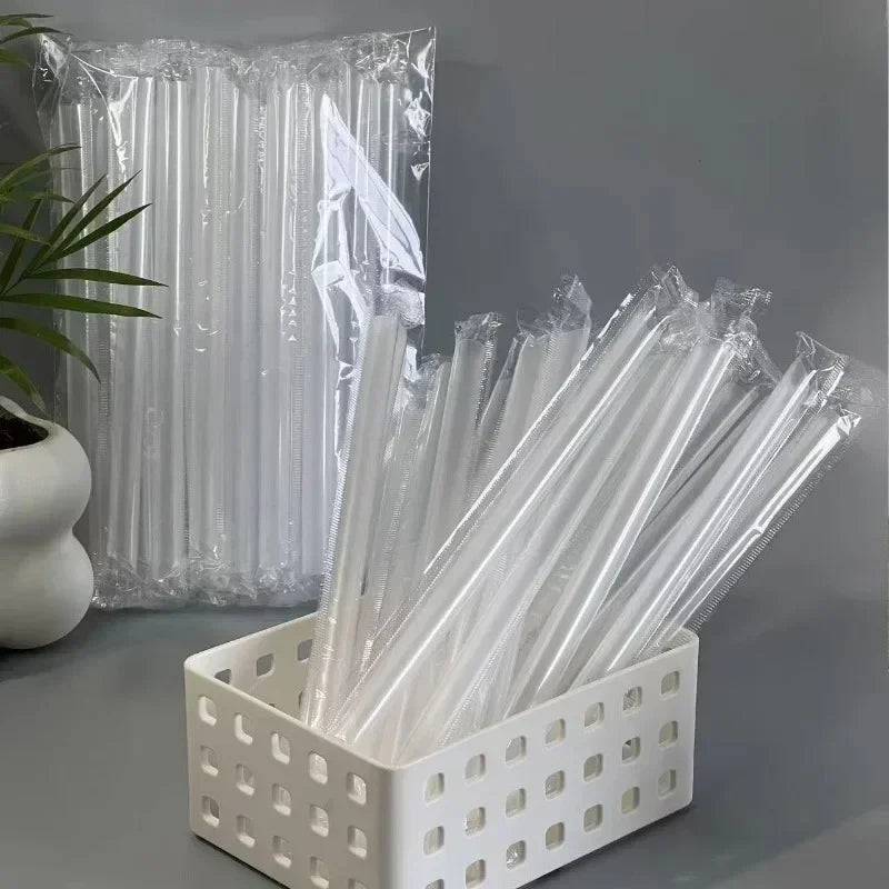 A collection of clear disposable plastic straws stored in a white grid container next to a plastic bag.