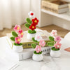 A display of hand woven crochet flowers in various shades of pink and red potted in white ceramic containers.
