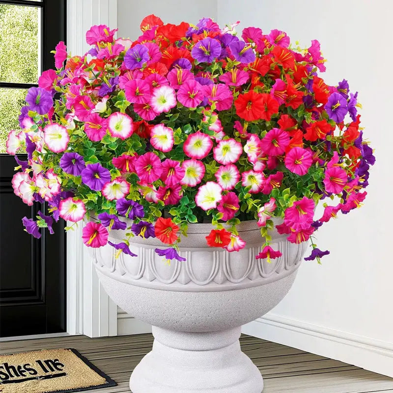 A vibrant bouquet of artificial silk cloth flowers in shades of pink, red, and purple displayed in a white urn.