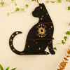 A black silhouette of a cat with gold accents and stars, mounted on a wall shelf surrounded by green vines.